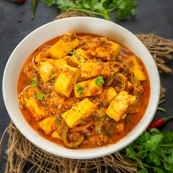 A white bowl filled with paneer curry, garnished with fresh cilantro, on a dark surface.